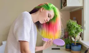 Jeune femme aux cheveux multicolores, elle se prépare à refaire une couleur par-dessus une couleur, avec une brosse à la main.
