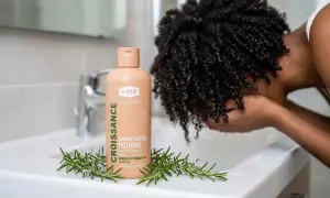 Shampoing "Croissance Pousse" WAAM, avec romarin, pour aider à comment faire pousser les cheveux. Une personne aux cheveux bouclés se lave le visage.