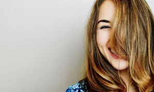 Une jeune femme rit, ses cheveux eclaircis tombant sur son visage.
