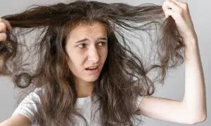 Jeune femme aux cheveux bruns et indisciplinés, se demandant comment faire pour que les cheveux ne gonflent pas. Elle tire sur une mèche, l'air frustrée.