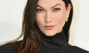 Une femme aux cheveux bruns foncés arbore une coloration claire subtile, sans décoloration visible, rehaussée par un col roulé noir et des boucles d'oreilles dorées.