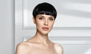 Une femme au regard intense arbore une coupe au bol audacieuse, ses cheveux noirs encadrant son visage aux traits fins.