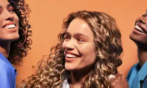Trois femmes souriantes aux cheveux bouclés, chacune avec un style unique. Une inspiration pour savoir quelle frange pour quel visage.