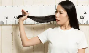Femme mesurant sa longue chevelure noire devant une règle graduée, peut-être pour suivre le ralentir pousse cheveux.