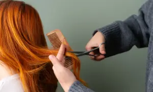 Une personne se coupe les cheveux roux avec des ciseaux, comme si elle se coupait les cheveux avec la lune.