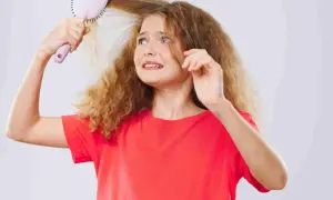 Une jeune fille aux cheveux mousseux et fins essaie de se brosser les cheveux, l'air désemparée.
