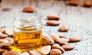 Huile d'amande dorée dans un petit pot, entourée d'amandes. Un secret naturel pour le bienfait des amandes sur les cheveux.