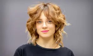 Une femme au regard bleu et aux lèvres roses arbore une coupe wolf cut dégradée et texturisée, un style audacieux et moderne.