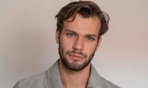 Un homme aux yeux bleus perçants arbore une coupe homme cheveux raides, légèrement ondulés sur le dessus, et une barbe courte.