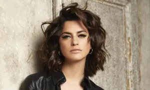 Une femme au regard intense, avec une coupe de cheveux pour visage carré qui encadre joliment ses traits. Elle porte une veste en cuir noire.