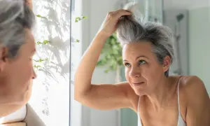 Une femme regarde ses cheveux poivre et sel dans le miroir, se demandant comment les blanchir pour un look plus lumineux.