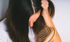 Une femme observe une brosse à cheveux remplie de cheveux, signe d'une possible chute de cheveux en automne.