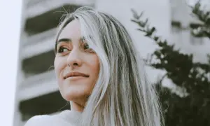 Portrait d'une jeune femme aux cheveux blonds, avec une transition grey blending subtile. Elle regarde au loin, un léger sourire aux lèvres.
