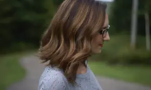 Profil d'une femme aux cheveux châtain avec des mèches blanches, portant des lunettes.