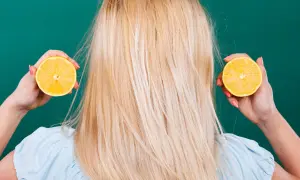 Une femme aux cheveux blonds tient des moitiés de citron près de ses oreilles, suggérant des aliments mauvais pour les cheveux.