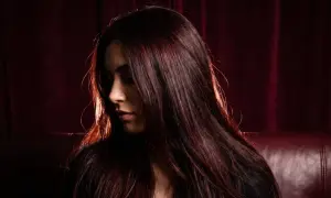 Chevelure brune aux reflets auburn, une femme pose, son visage tourné, comme pour éclaircir cheveux noir sans décoloration.