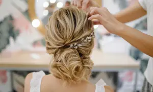 Une mariée se fait coiffer un chignon bouclé flou, orné d'une barrette scintillante.