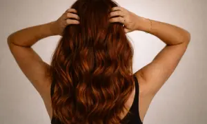 Vue arrière d'une femme aux cheveux ondulés d'une magnifique couleur cheveux auburn, ses mains dans sa chevelure.