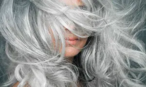 Gros plan sur une femme aux cheveux poivre et sel naturels, une chevelure argentée et volumineuse qui encadre son visage.