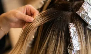 Main d'une coiffeuse travaillant sur des mèches de cheveux, comparant le foilyage et le balayage pour un effet naturel.