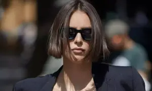 Une femme porte des lunettes de soleil et une veste, ses cheveux arborent une coupe carré court dégradé effilé.