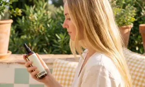 Une femme aux cheveux blonds tient un flacon. Elle cherche à éclaircir ses cheveux naturellement avec ce produit.