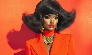 Une femme arbore une coiffure année 70 volumineuse et des bijoux éclatants, vêtue d'un blazer orange vif.