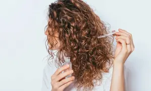 Une femme applique une huile sur ses cheveux bouclés pour définir ses frisottis.