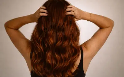 Vue arrière d'une femme aux cheveux ondulés d'une magnifique couleur cheveux auburn, ses mains dans sa chevelure.