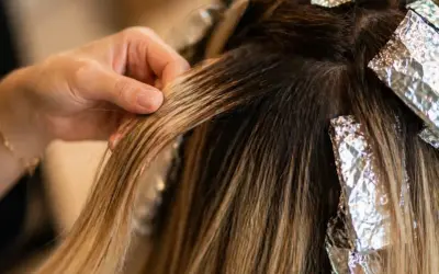 Main d'une coiffeuse travaillant sur des mèches de cheveux, comparant le foilyage et le balayage pour un effet naturel.