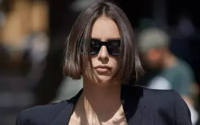 Une femme porte des lunettes de soleil et une veste, ses cheveux arborent une coupe carré court dégradé effilé.