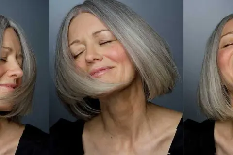 Une femme de 60 ans au visage ovale arbore une coupe de cheveux courte et grisonnante, exprimant joie et sérénité.