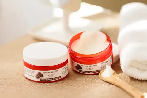 Deux pots de beurre de karité, parfaits pour les bienfaits cheveux. Une cuillère en bois en présente la texture onctueuse.