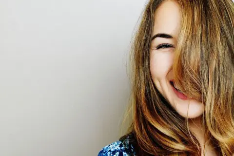 Une jeune femme rit, ses cheveux eclaircis tombant sur son visage.