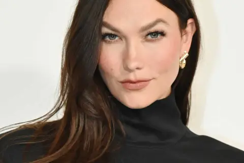 Une femme aux cheveux bruns foncés arbore une coloration claire subtile, sans décoloration visible, rehaussée par un col roulé noir et des boucles d'oreilles dorées.
