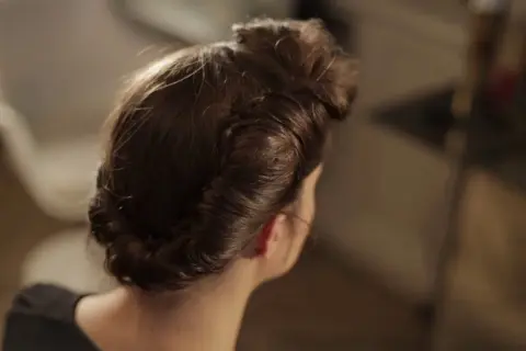 Coiffure année 50 élégante, avec des boucles et un chignon bas, rappelant le glamour d'une autre époque.