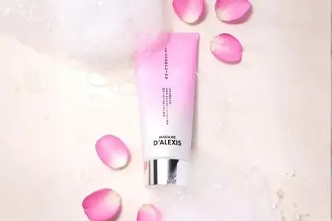 Tube de shampooing rose et blanc, entouré de pétales de rose et de bulles. Idéal pour espacer les shampoings et hydrater vos cheveux.