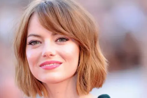 Emma Stone, avec sa coupe de cheveux courte et ondulée, met en valeur son visage rond et ses grands yeux verts.