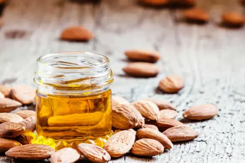 Huile d'amande dorée dans un petit pot, entourée d'amandes. Un secret naturel pour le bienfait des amandes sur les cheveux.