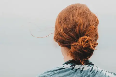 Chevelure rousse coiffée en un chignon facile, quelques mèches s'échappent dans la brise légère.