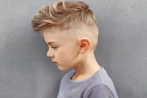 Un jeune garçon de 8 ans arbore une coupe de cheveux moderne avec un dégradé sur les côtés et des mèches blondes texturées sur le dessus.