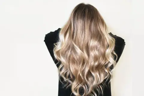 Cheveux châtain transformés en une cascade de mèches blondes lumineuses, un éclaircissement subtil pour un look naturel et ensoleillé.