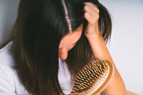 Une femme observe une brosse à cheveux remplie de cheveux, signe d'une possible chute de cheveux en automne.