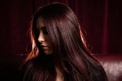 Chevelure brune aux reflets auburn, une femme pose, son visage tourné, comme pour éclaircir cheveux noir sans décoloration.