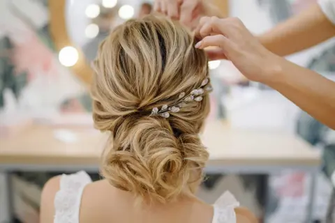 Une mariée se fait coiffer un chignon bouclé flou, orné d'une barrette scintillante.