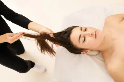 Une femme reçoit un massage du cuir chevelu pour stimuler la pousse des cheveux. Ses yeux sont fermés, elle est détendue.