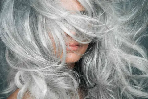 Gros plan sur une femme aux cheveux poivre et sel naturels, une chevelure argentée et volumineuse qui encadre son visage.