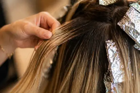 Main d'une coiffeuse travaillant sur des mèches de cheveux, comparant le foilyage et le balayage pour un effet naturel.