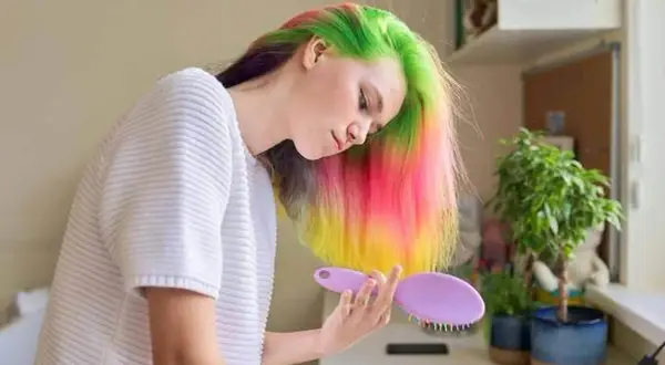 Jeune femme aux cheveux multicolores, elle se prépare à refaire une couleur par-dessus une couleur, avec une brosse à la main.