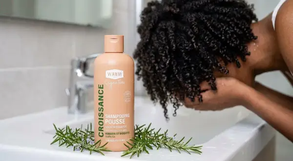 Shampoing "Croissance Pousse" WAAM, avec romarin, pour aider à comment faire pousser les cheveux. Une personne aux cheveux bouclés se lave le visage.
